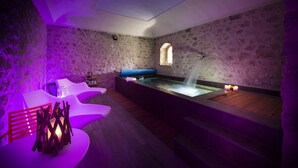 A spa room with a stone wall, a wooden bench, a massage table, and a small window.