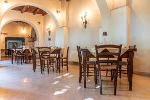 Un comedor con varias mesas y sillas, techos abovedados y lámparas fijadas a la pared.