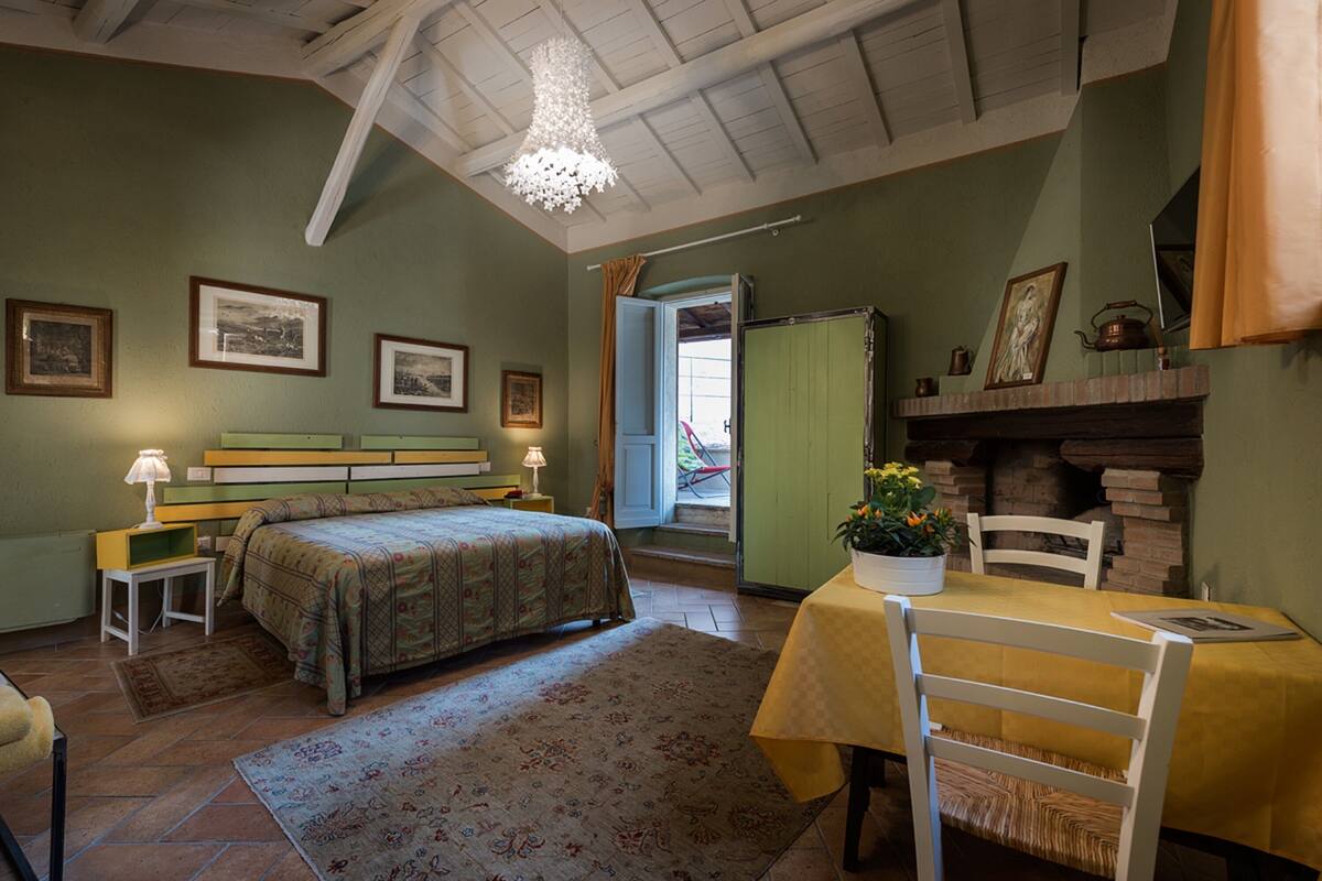 Een slaapkamer met een bed, nachtkastjes, een kaptafel, een stoel, een tafel met een gele tafelkleed en een open haard.