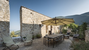 An outdoor patio with stone walls, a table, chairs, and a large umbrella.