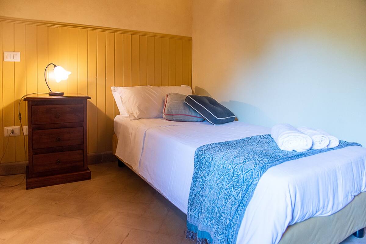 Een slaapkamer met een bed, nachtkastje, lamp en een houten dressoir.