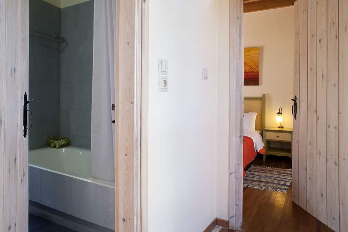 Casa de banho com chuveiro e banheira, quarto com cama e mesa de cabeceira, e chão de madeira.