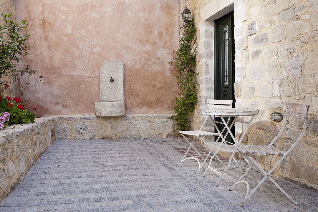 A stone courtyard with a tiled floor, a white metal table and chair, and a door with a green frame.