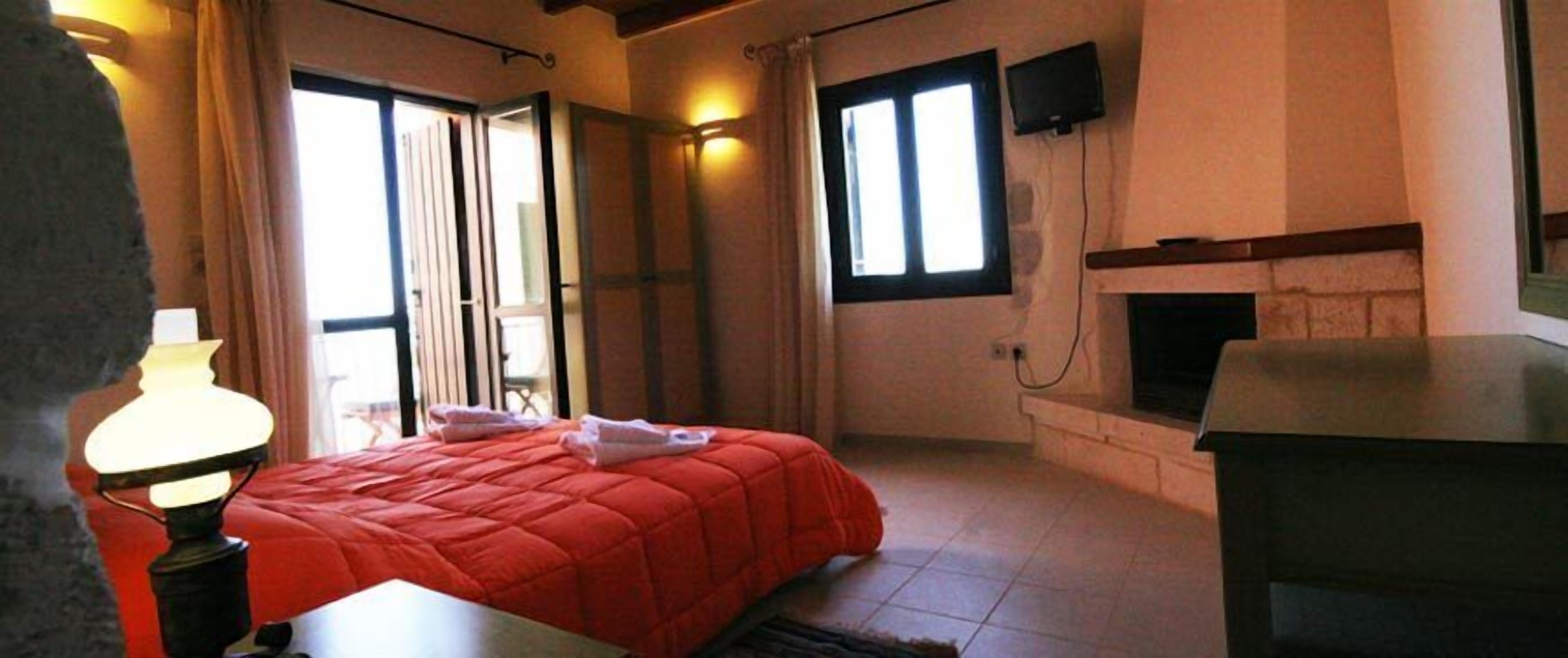 A hotel room with a bed, a fireplace, a TV, and a window.