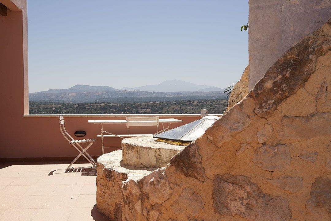 A balcony with a view of distant mountains, a table, and a chair.