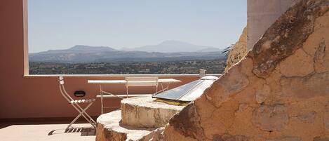A balcony with a view of distant mountains, a table, and a chair.