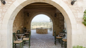 An outdoor patio with stone flooring, green chairs, and a stone table under an archway. - Kastellos Village - Central Complex (Apokoronas)