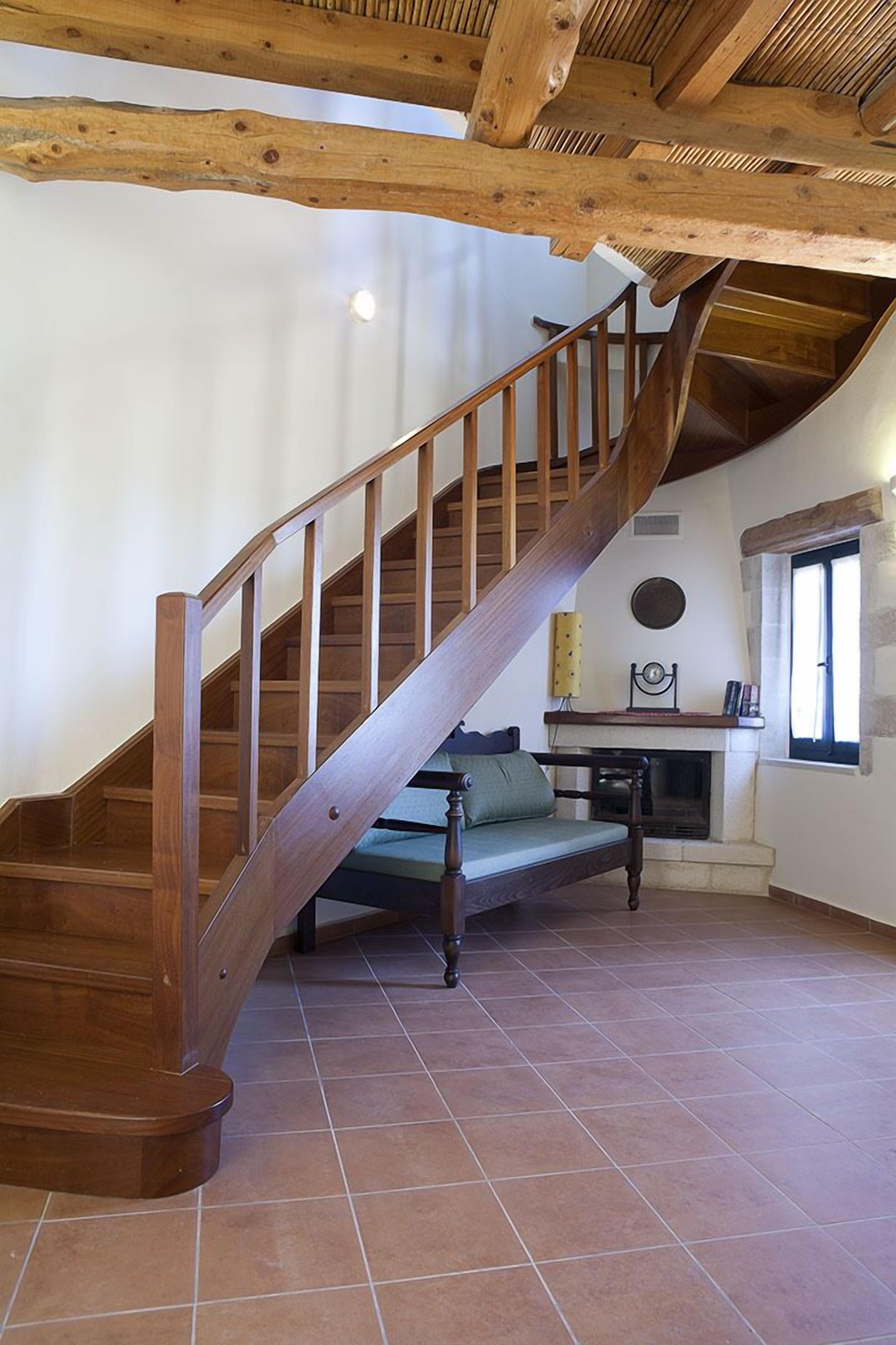 Un escalier en bois mène à une chambre située en mezzanine, où se trouvent un canapé vert et une cheminée.