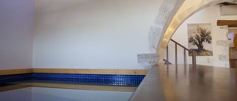 A spacious indoor swimming pool with a tiled floor and a wooden deck area.