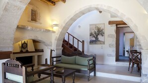 A rustic interior with a stone fireplace, wooden furniture, and a staircase leading to another room. - Kastellos Village - Central Complex (Apokoronas)