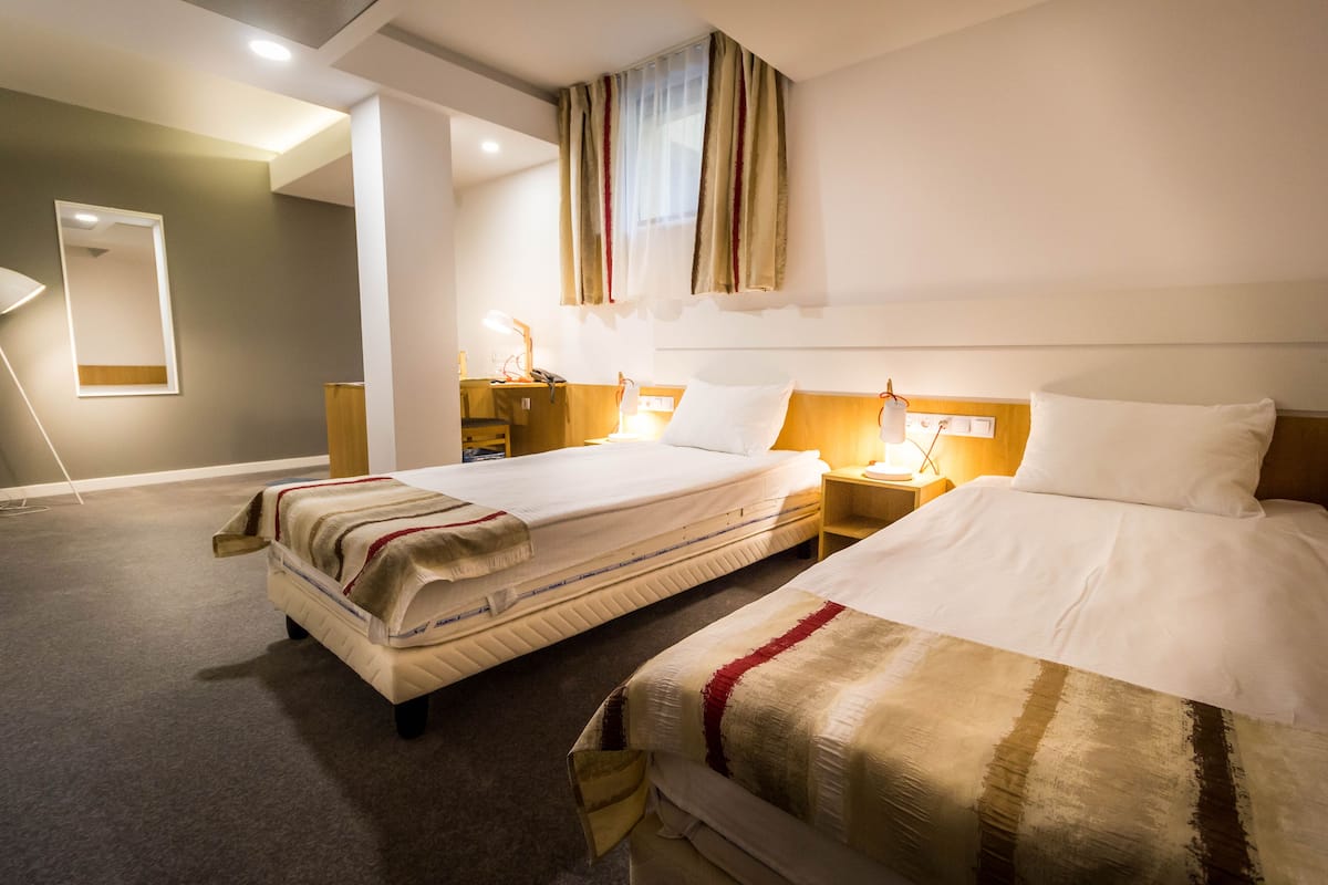 A hotel room with two beds, a nightstand with a lamp, a wooden headboard, and a mirror on the wall.