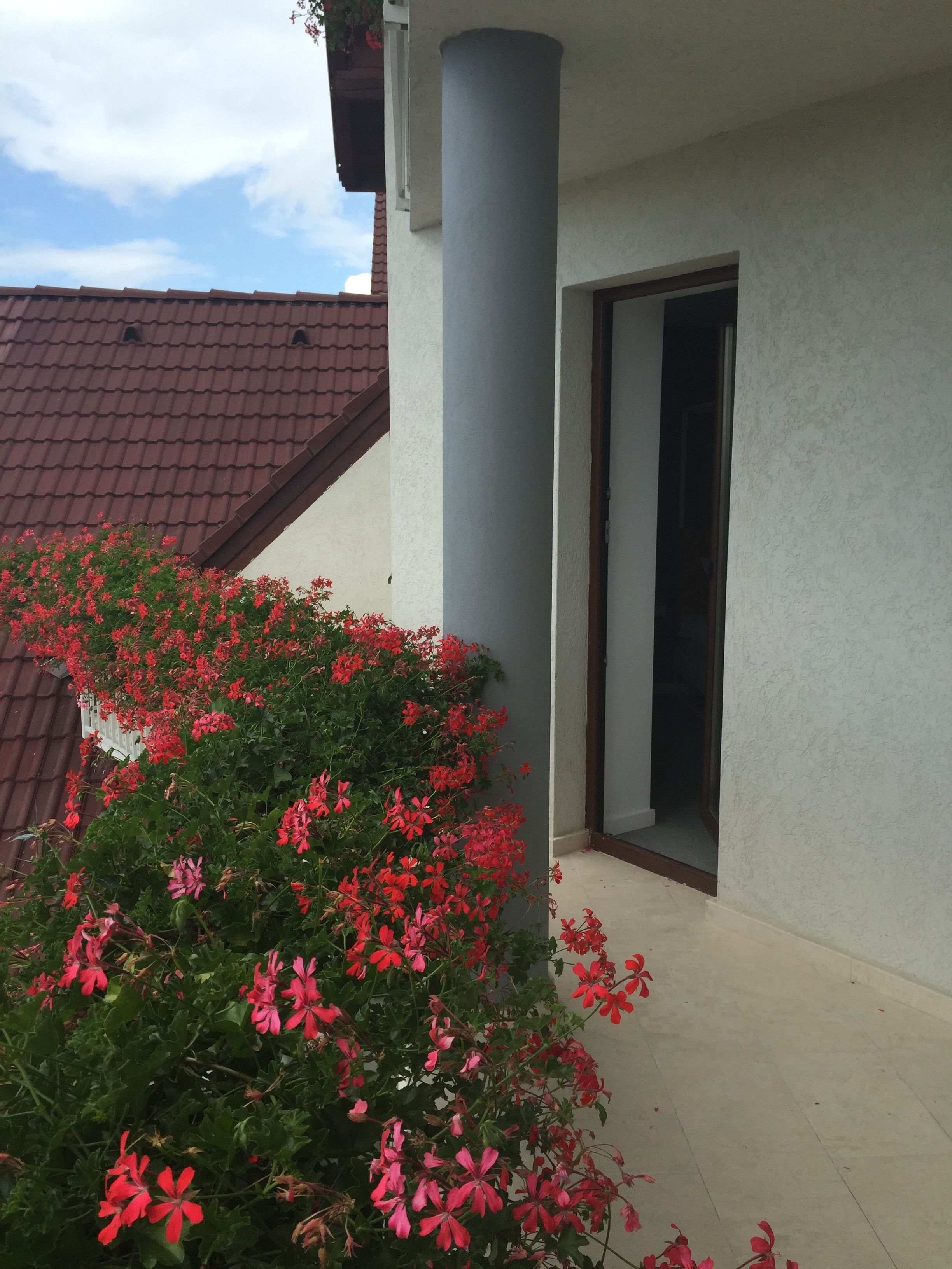 Un edificio con fachada gris, tejado de tejas rojas y un balcón adornado con flores rojas.