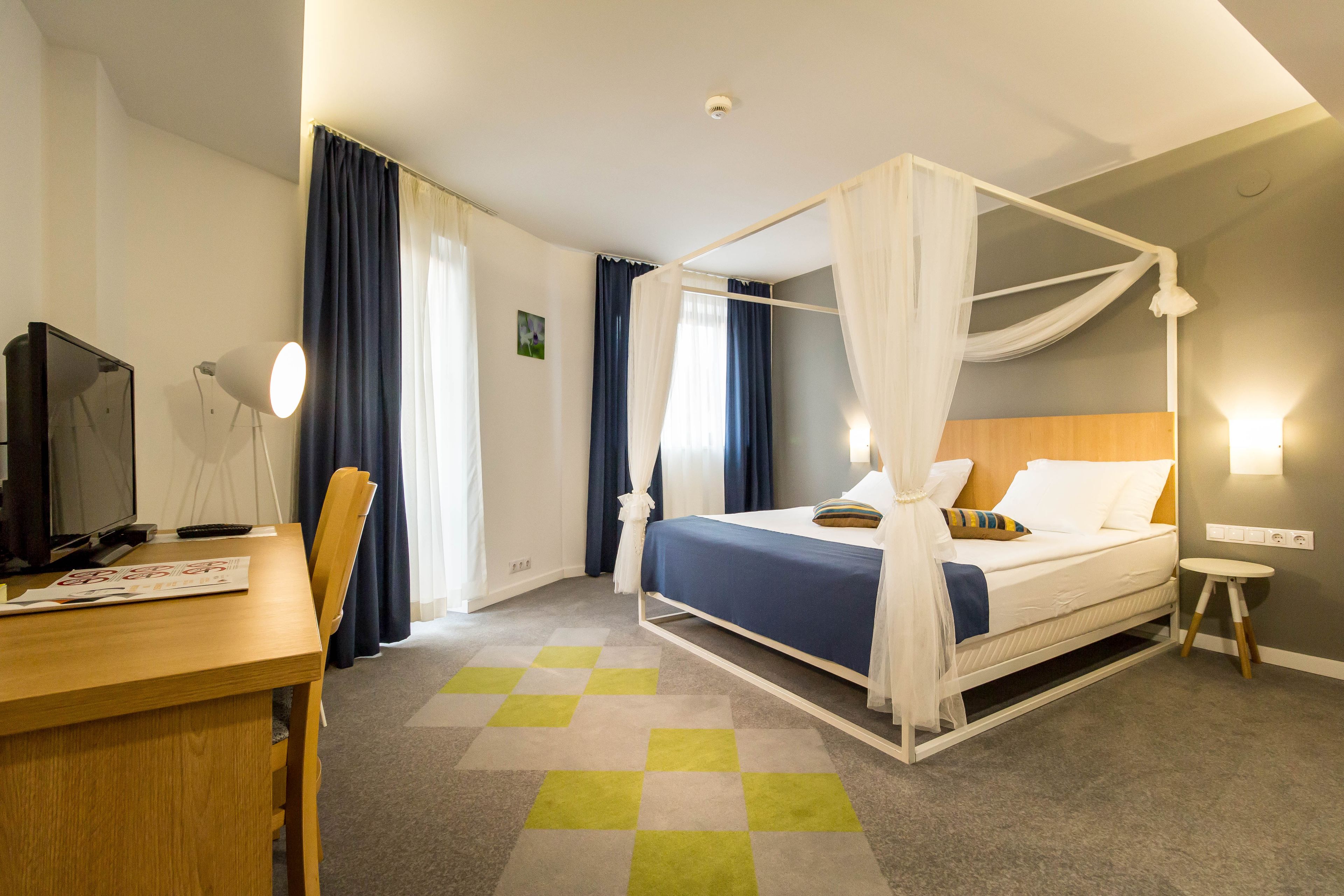 Quarto de hotel com uma cama de dossel, uma escrivaninha com computador e uma pequena mesa de cabeceira.