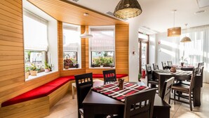 A restaurant with wooden panel walls, large windows with red cushioned seating, and a central dining table with a checkered table runner. - Horeum Boutique Hotel (Sura Mare)