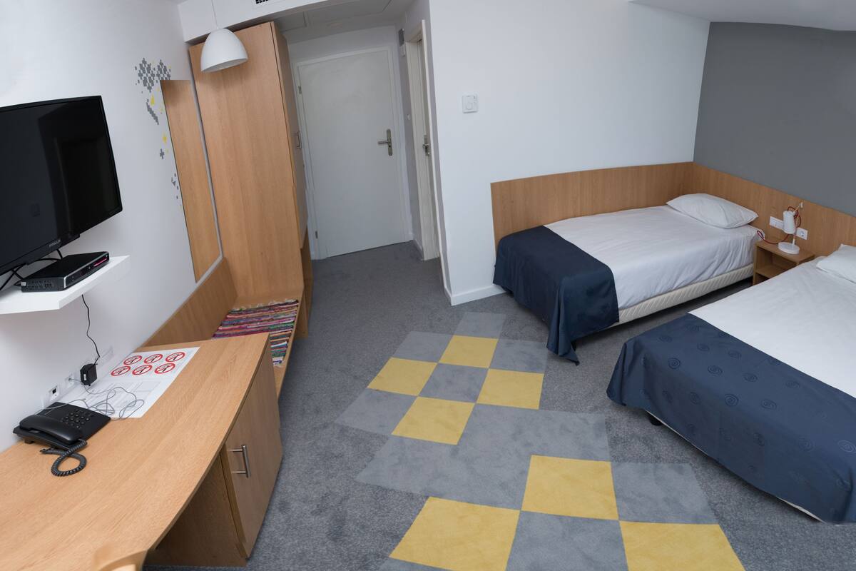 A hotel room with two beds, a desk with a phone, a TV, and a door leading to another room.