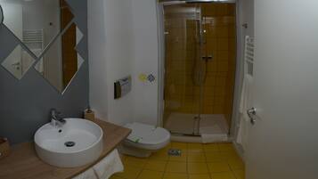 Un baño con lavamanos blanco, inodoro y cabina de ducha con paredes de vidrio.