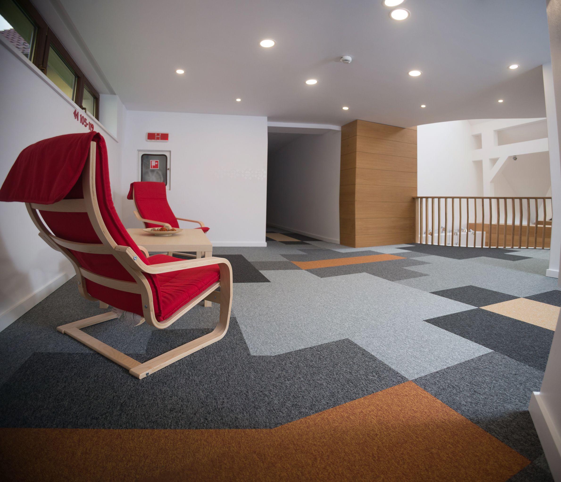 Una habitación de hotel moderna con una butaca reclinable roja, una mesita pequeña y una alfombra estampada.
