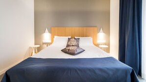 A neatly made bed with a dark blue bedspread and two decorative pillows, flanked by two bedside tables with lamps. - Horeum Boutique Hotel (Sura Mare)