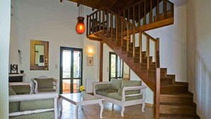 A spacious living area with a wooden staircase, a white coffee table, and two sofas. - Kastellos Village - Agathes Houses (Apokoronas)