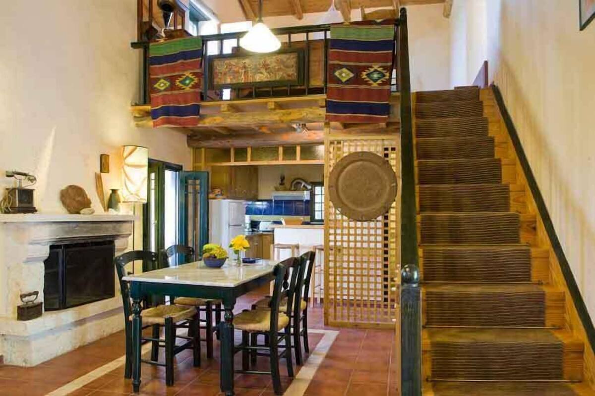 Un comedor con una mesa y sillas de madera, una chimenea y una escalera con baranda de madera.