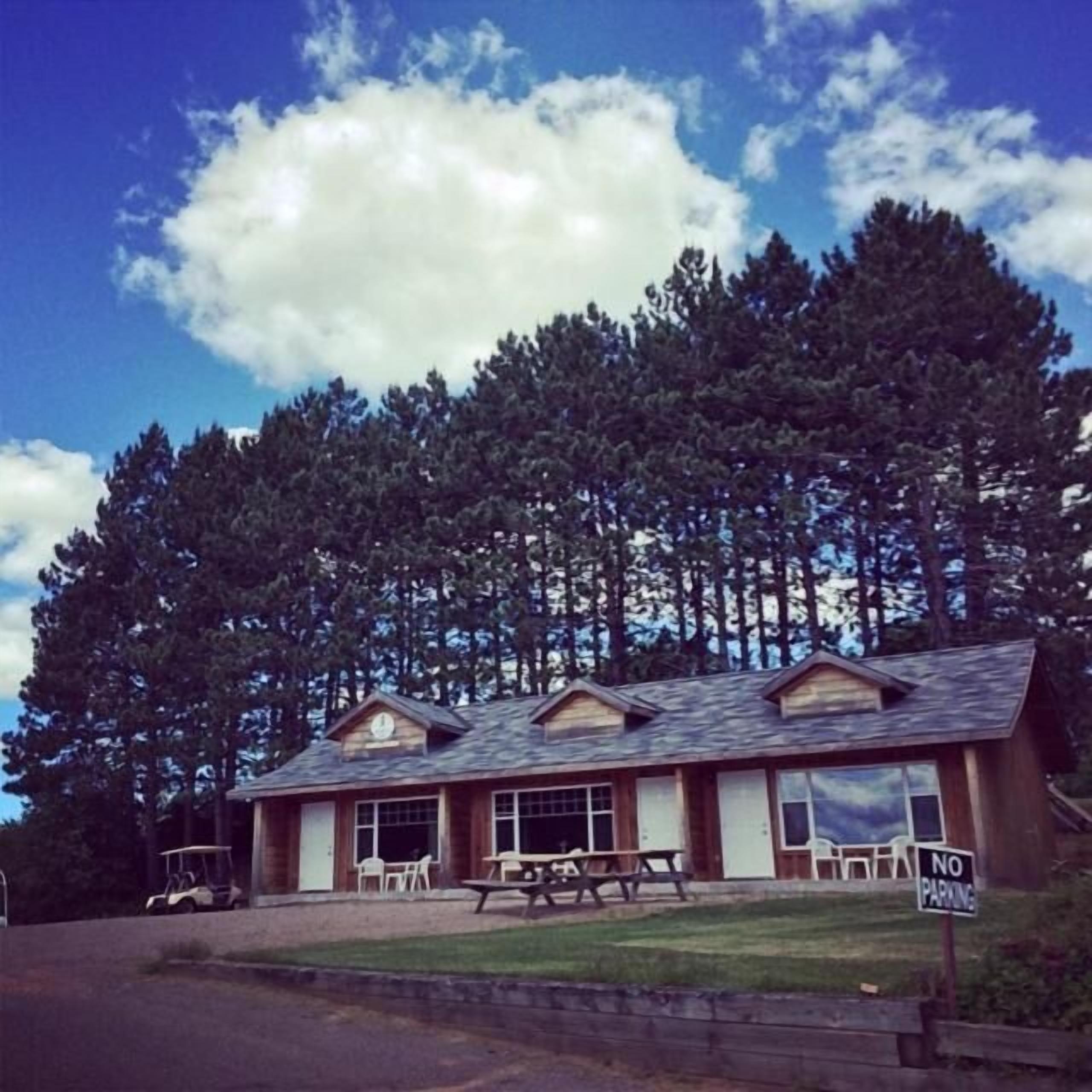 A lodge with a picnic table and chairs in front, surrounded by tall trees.
