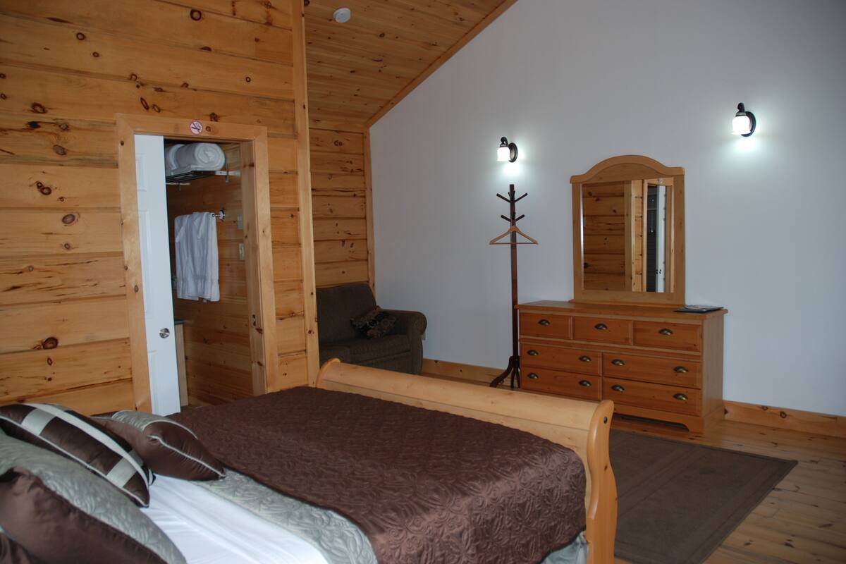 A wooden cabin bedroom with a bed, dresser, and a coat rack.