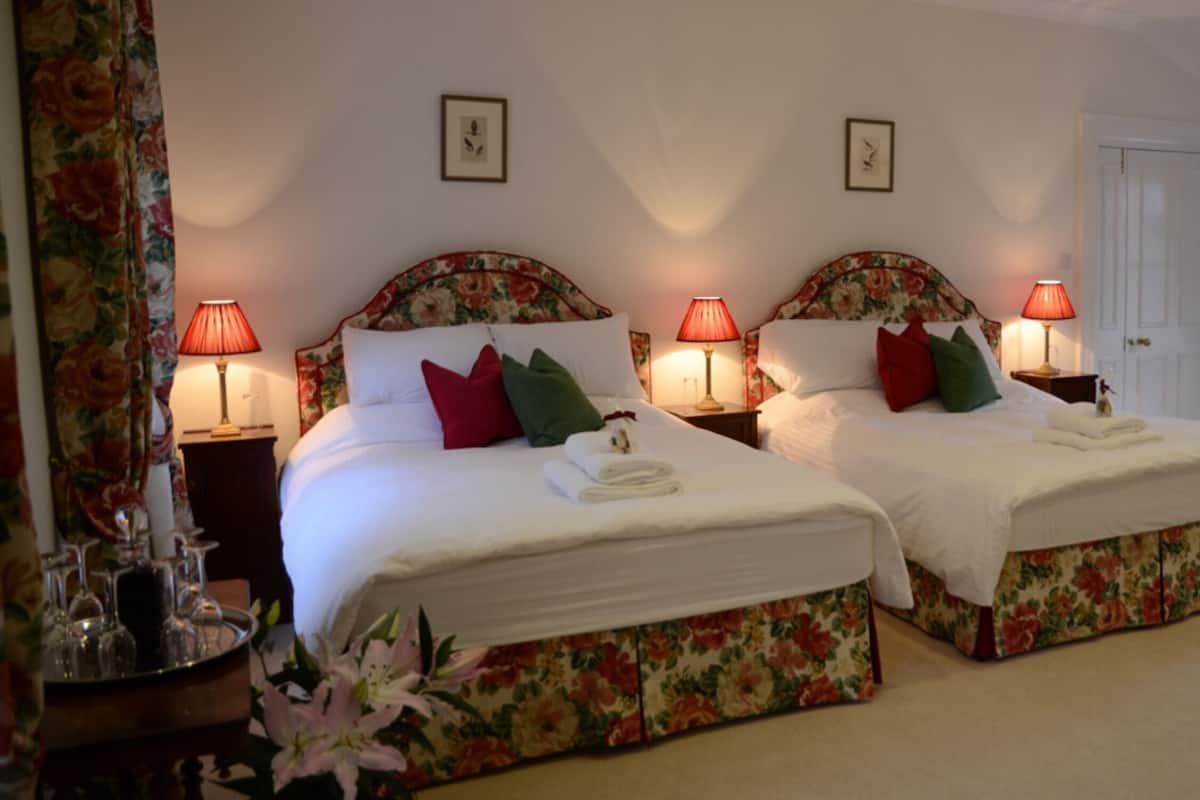 Ein Doppelzimmer mit zwei Betten, jeweils mit floralen Kopfteilen und Nachttischlampen.