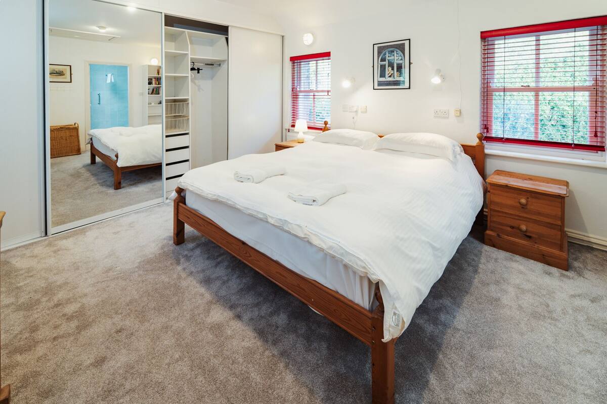 Ein Schlafzimmer mit einem großen Bett, einem Kleiderschrank, einem Nachttisch und einem Fenster mit Jalousien.