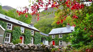 A stone wall with a stone house featuring a red door and windows, surrounded by greenery and a mountain in the background. - Delphi Lodge & Estate (Leenane)