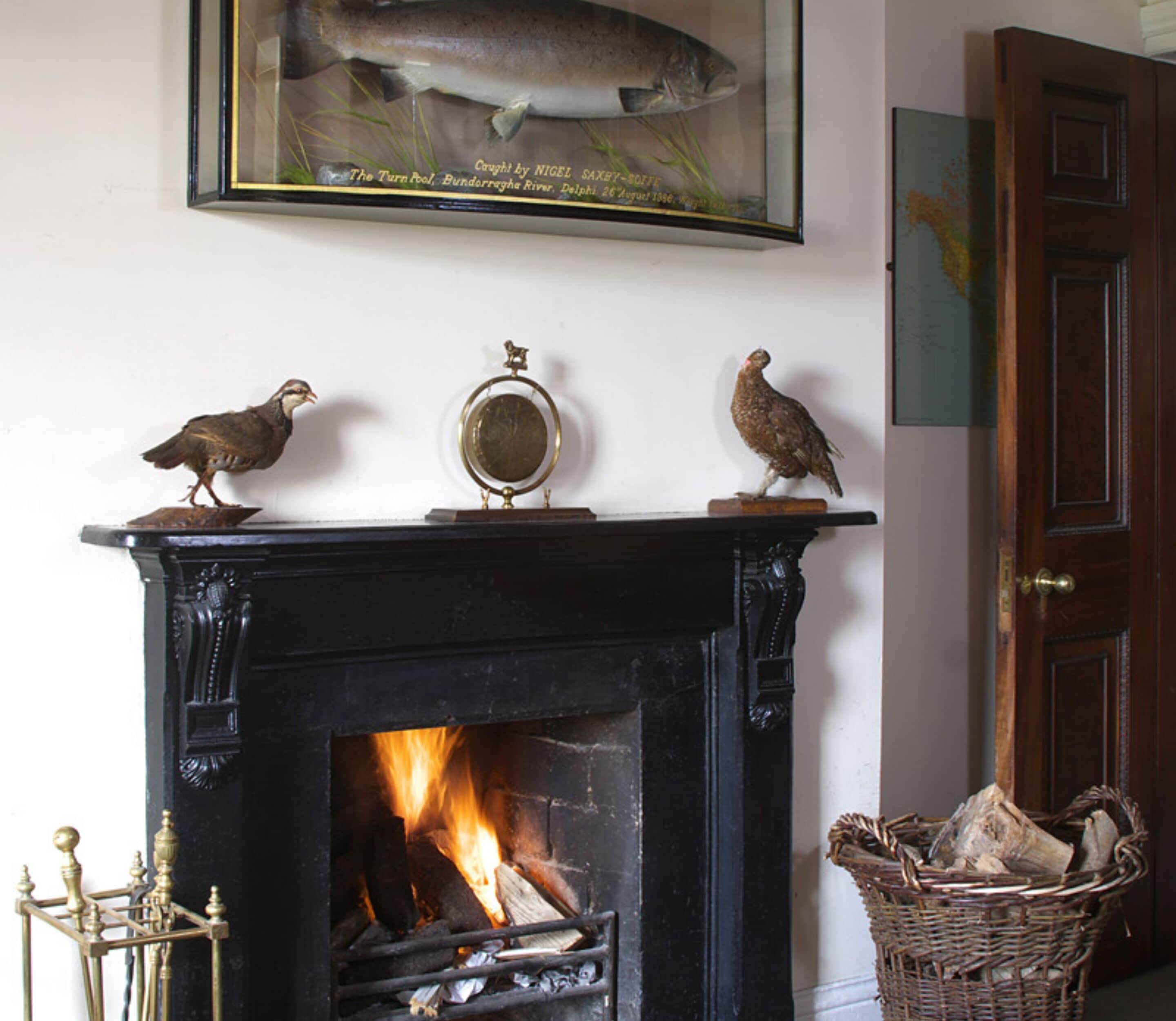 A fireplace with a fire, a framed fish, and two bird figurines on the mantel.