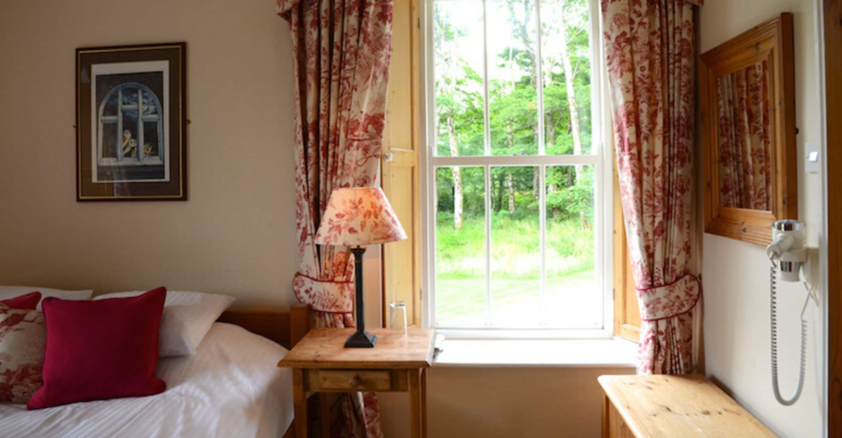 Une chambre à coucher avec un lit, une table de chevet avec une lampe, une fenêtre avec des rideaux et un téléphone.