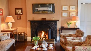 A living room with a fireplace, two sofas, a coffee table with tea set, and framed pictures on the wall. - Delphi Lodge & Estate (Leenane)
