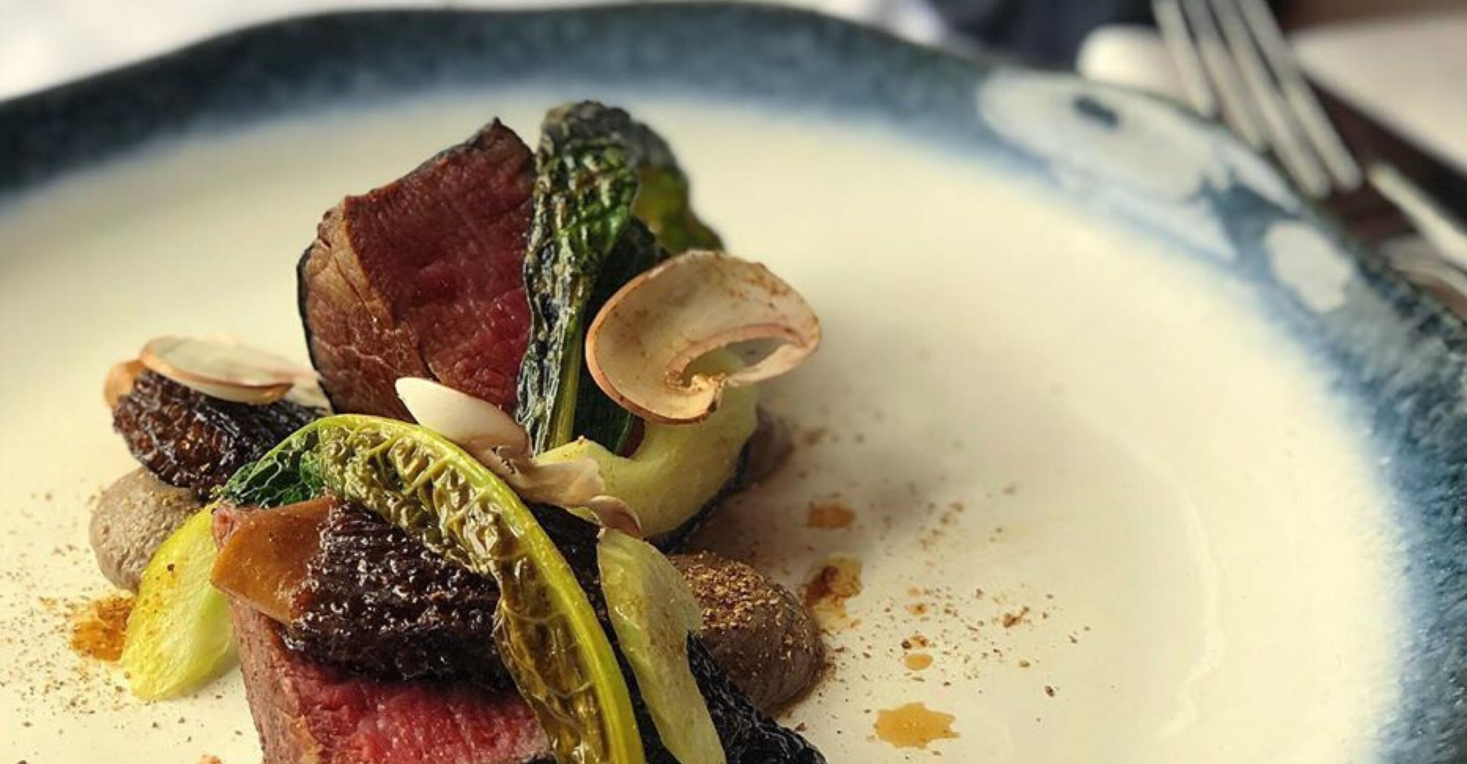 A plate with a steak, clams, and greens.
