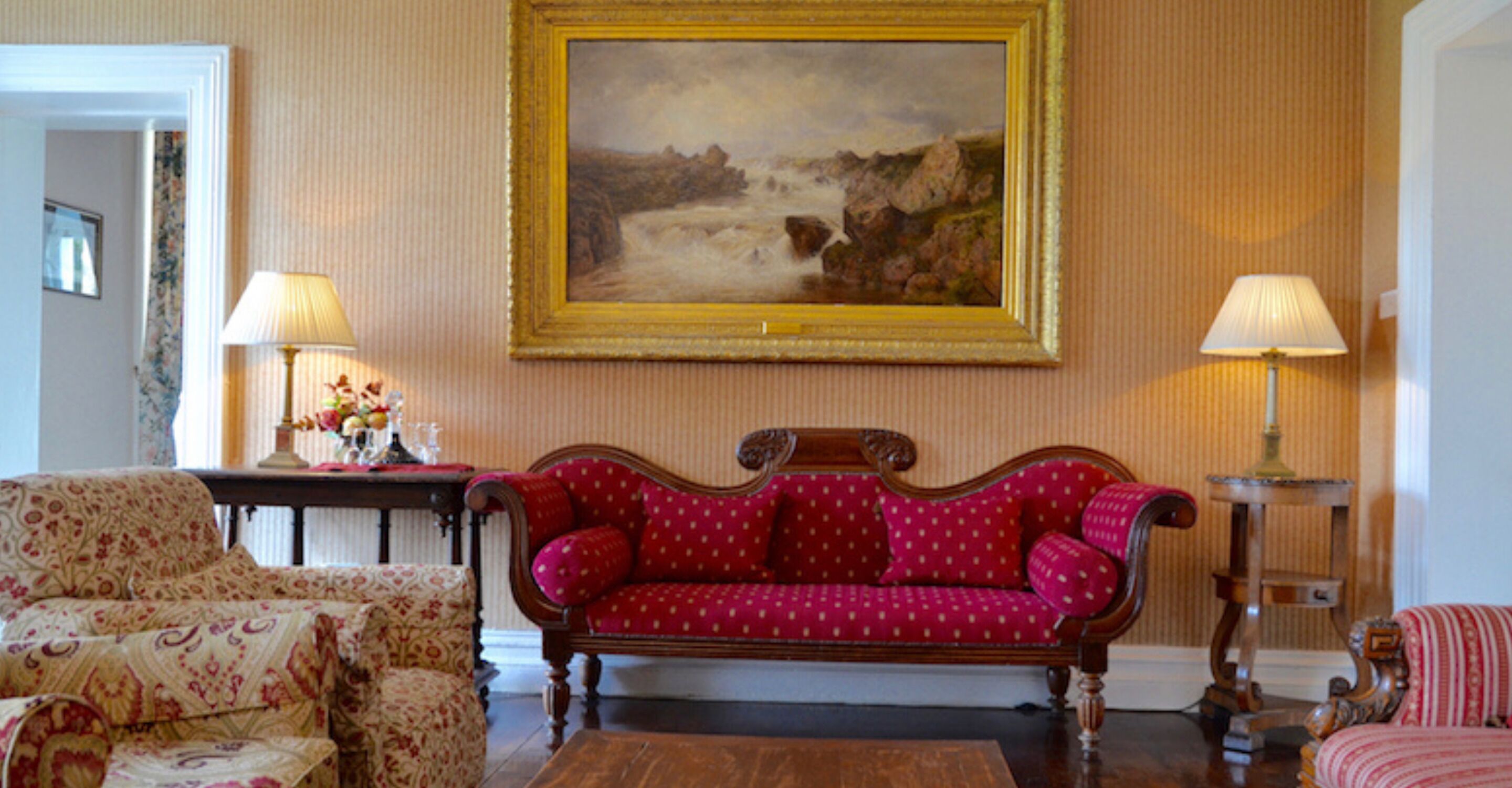 A living room with a red patterned sofa, two armchairs, a wooden coffee table, and a painting on the wall.