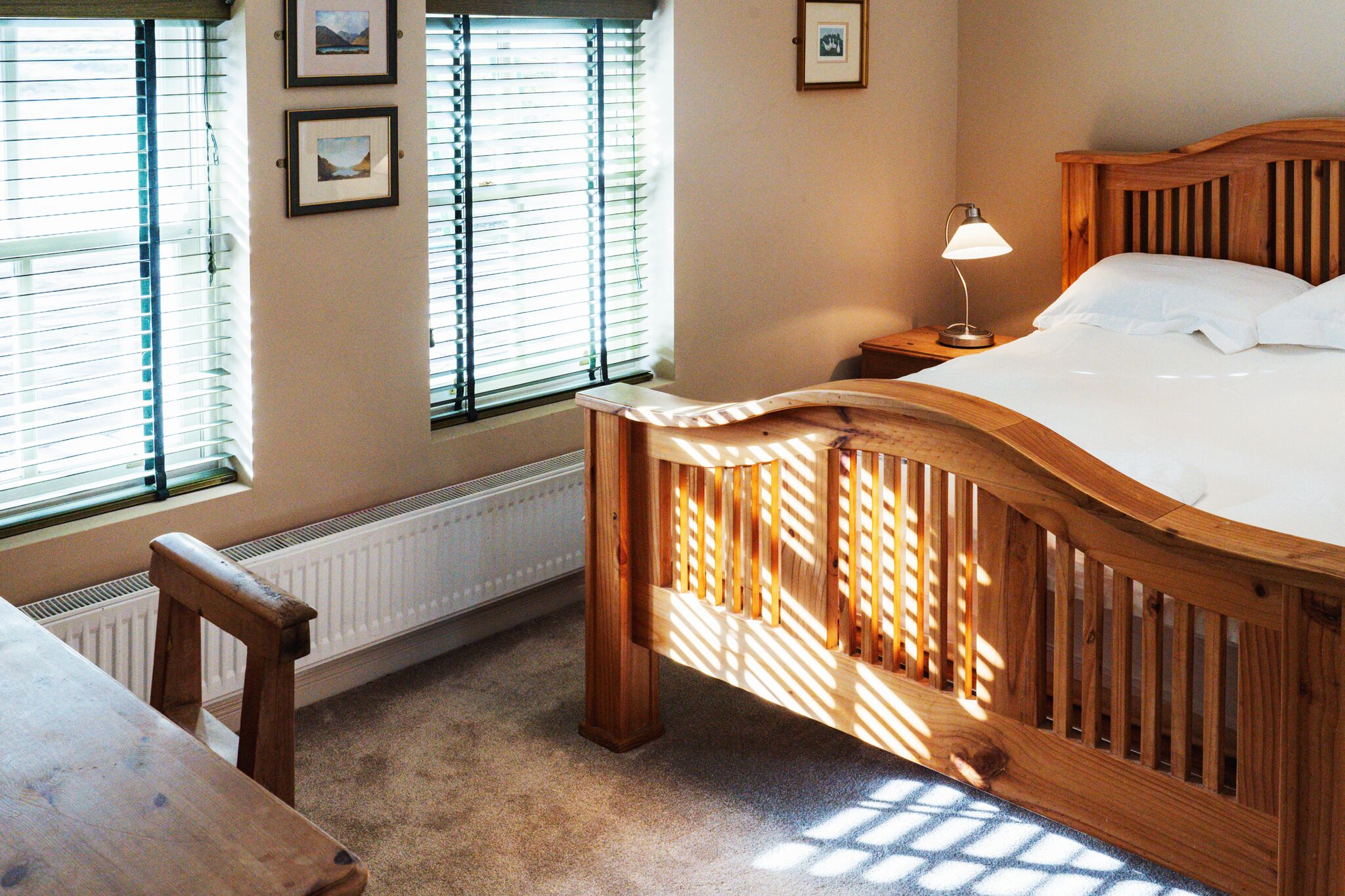 A bedroom with a wooden bed, a nightstand, a lamp, and a window with blinds.