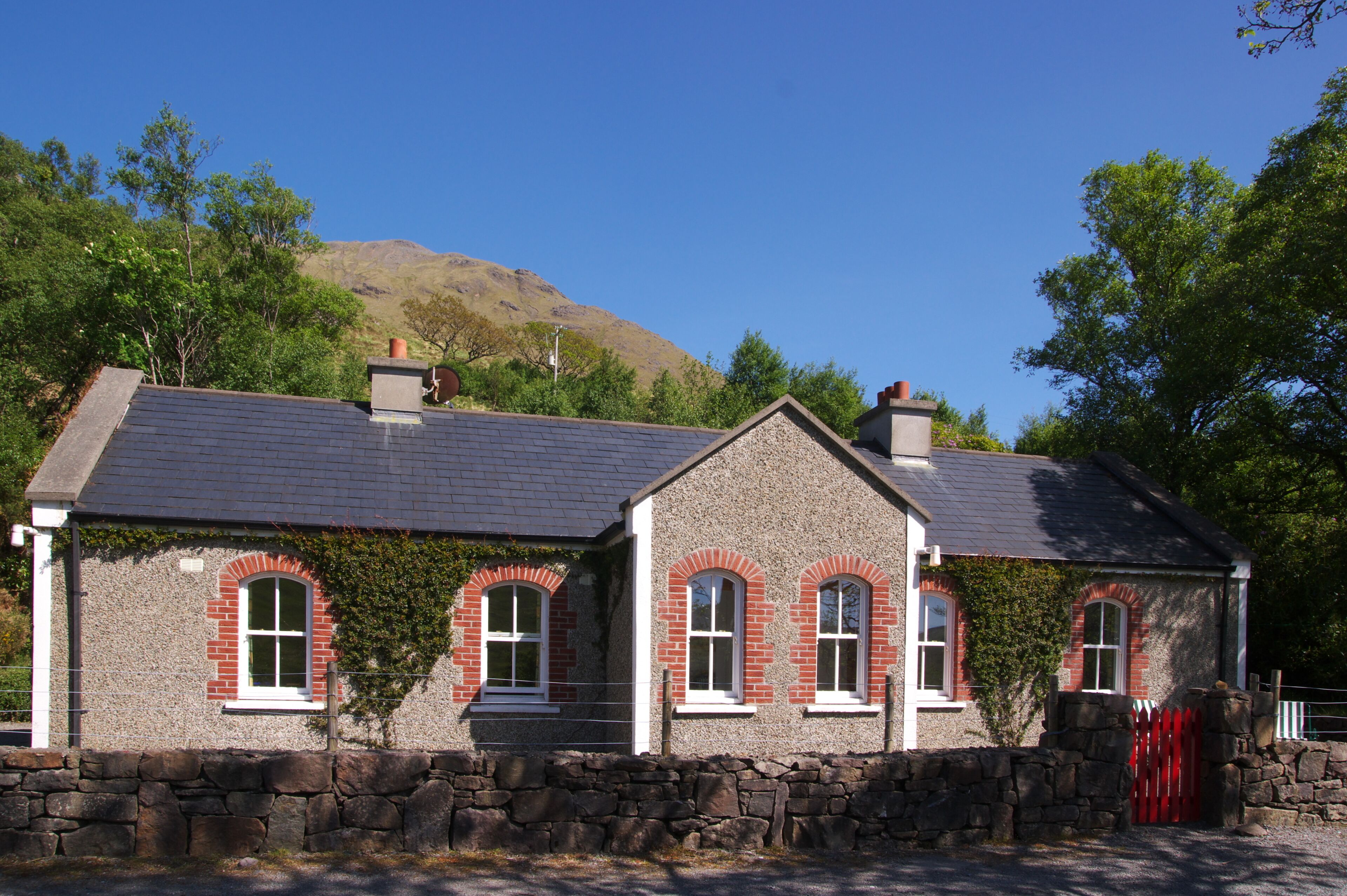 A stone house with a red door, white window frames, and a stone wall.