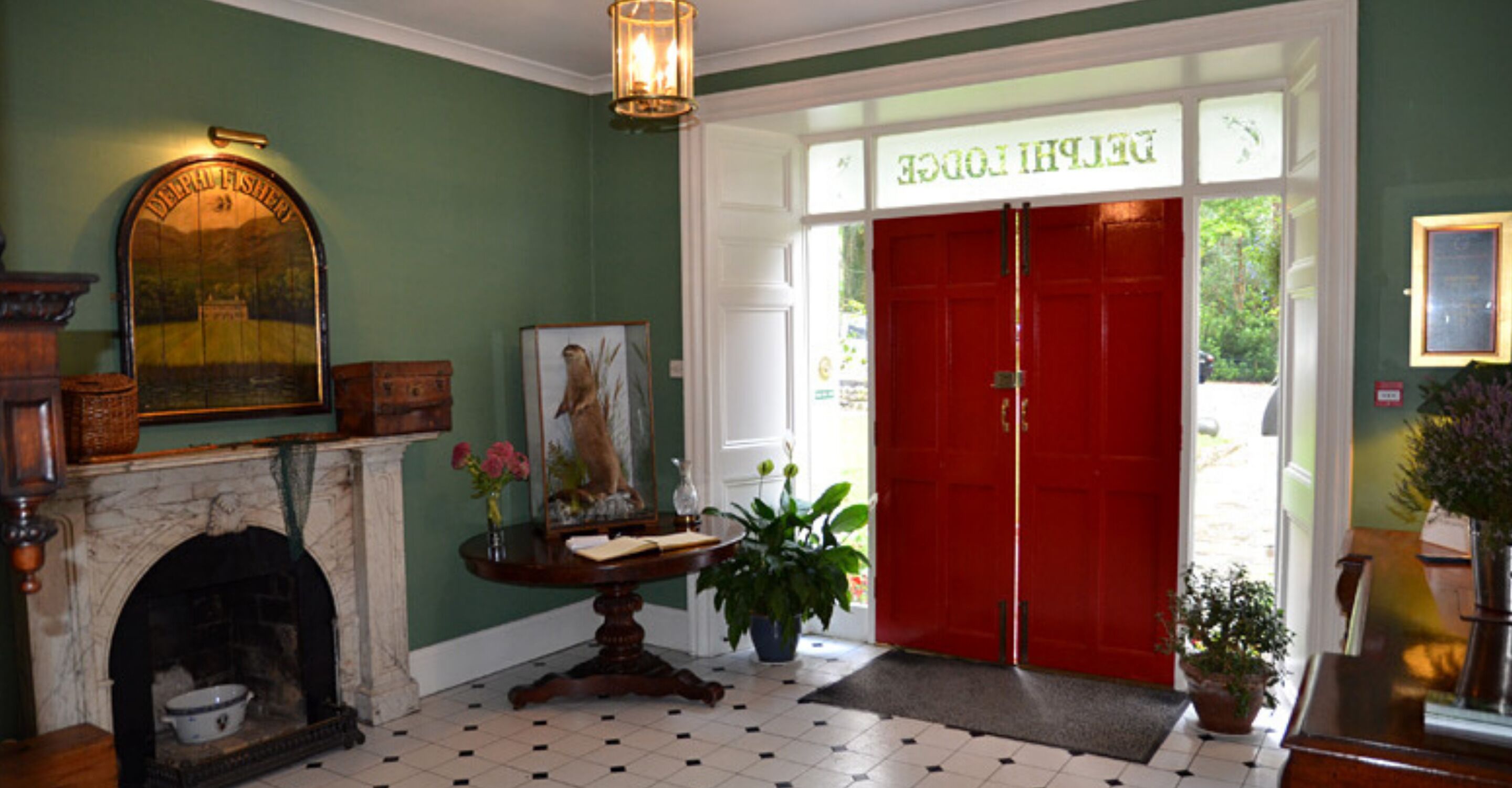 A hotel lobby with a fireplace, a round table with a vase of flowers, a red door, and a green wall.