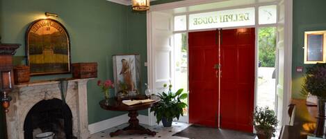 A hotel lobby with a fireplace, a round table with a vase of flowers, a red door, and a green wall.