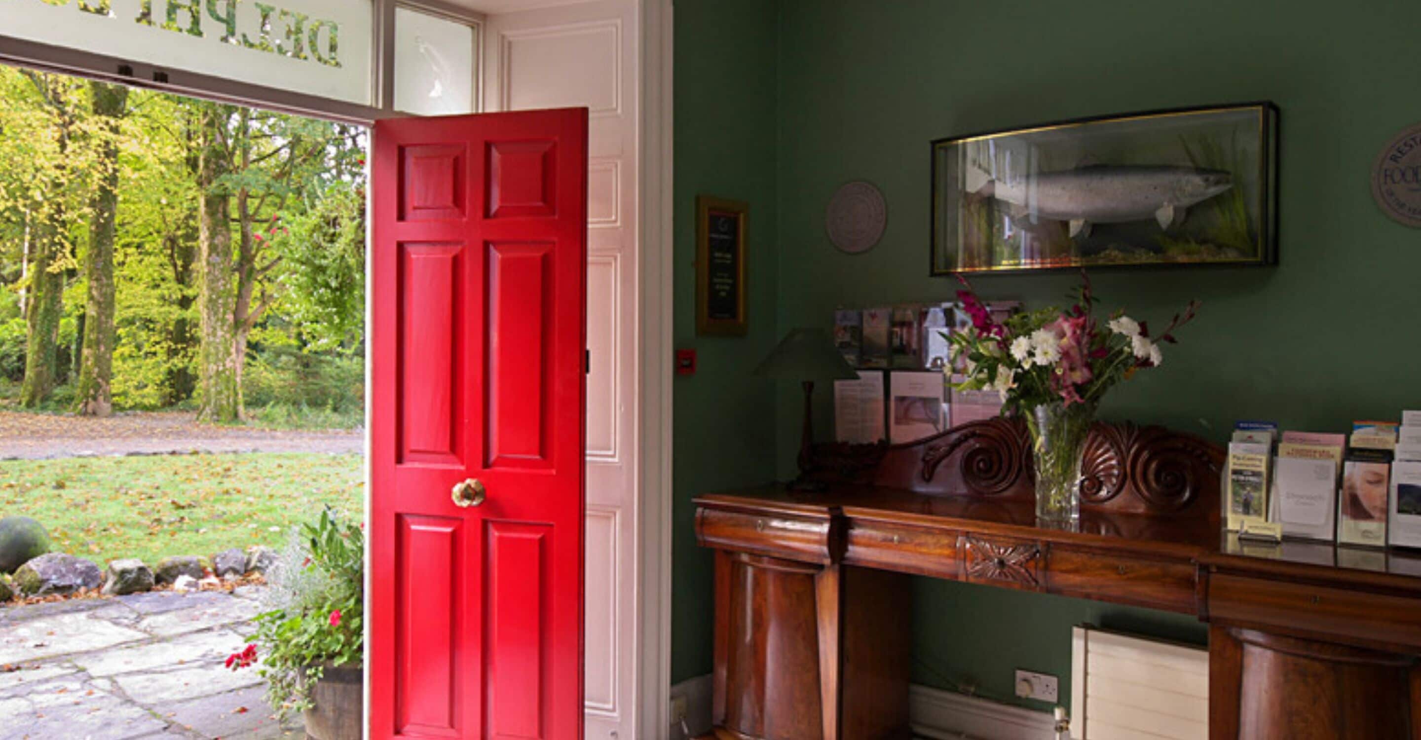 Une pièce avec une porte rouge, un bureau en bois orné d’un vase de fleurs et un tableau encadré accroché au mur.