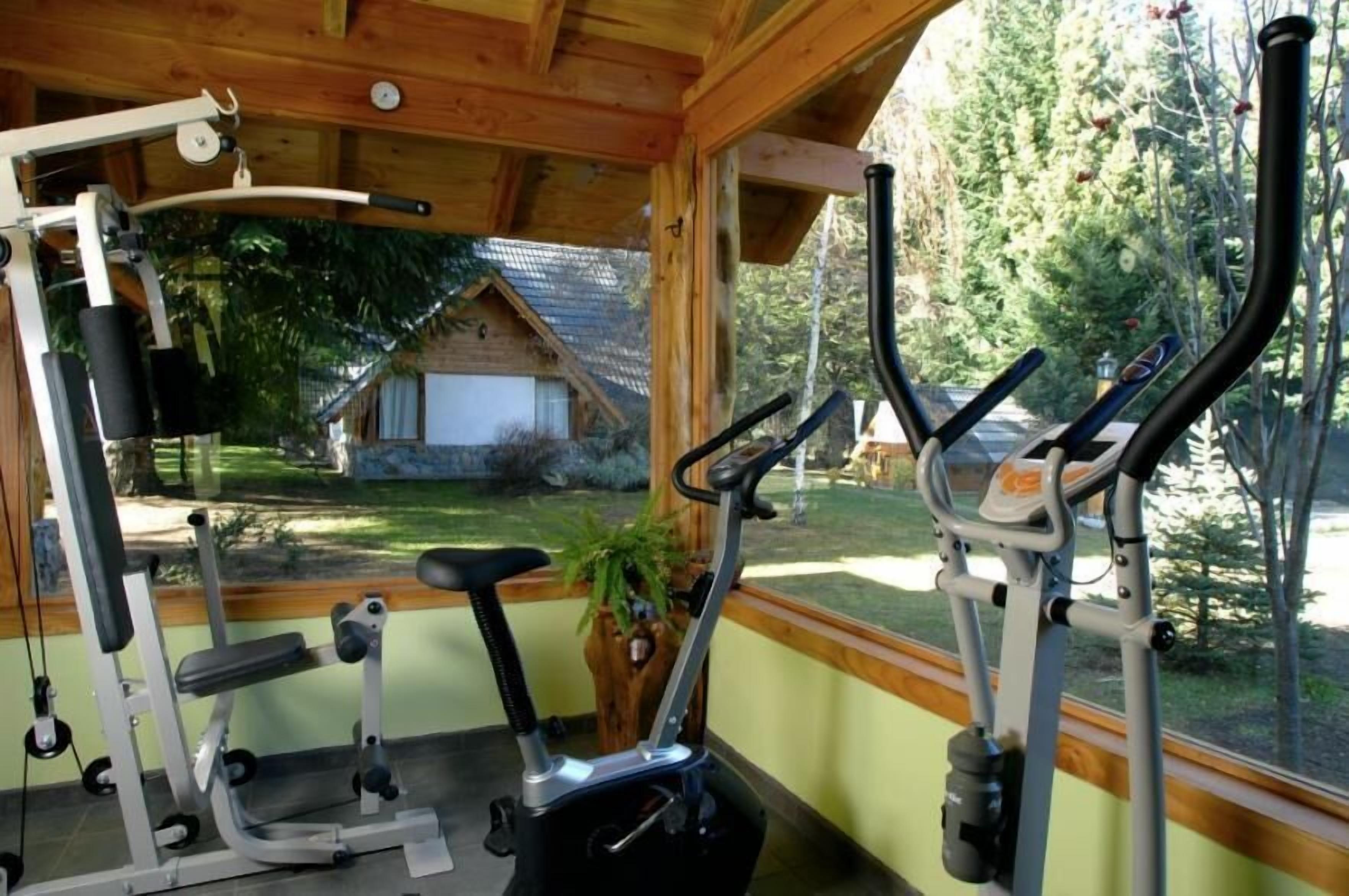 Une salle de sport équipée de matériel d’exercice, avec un banc et une vue sur une maison et des arbres.