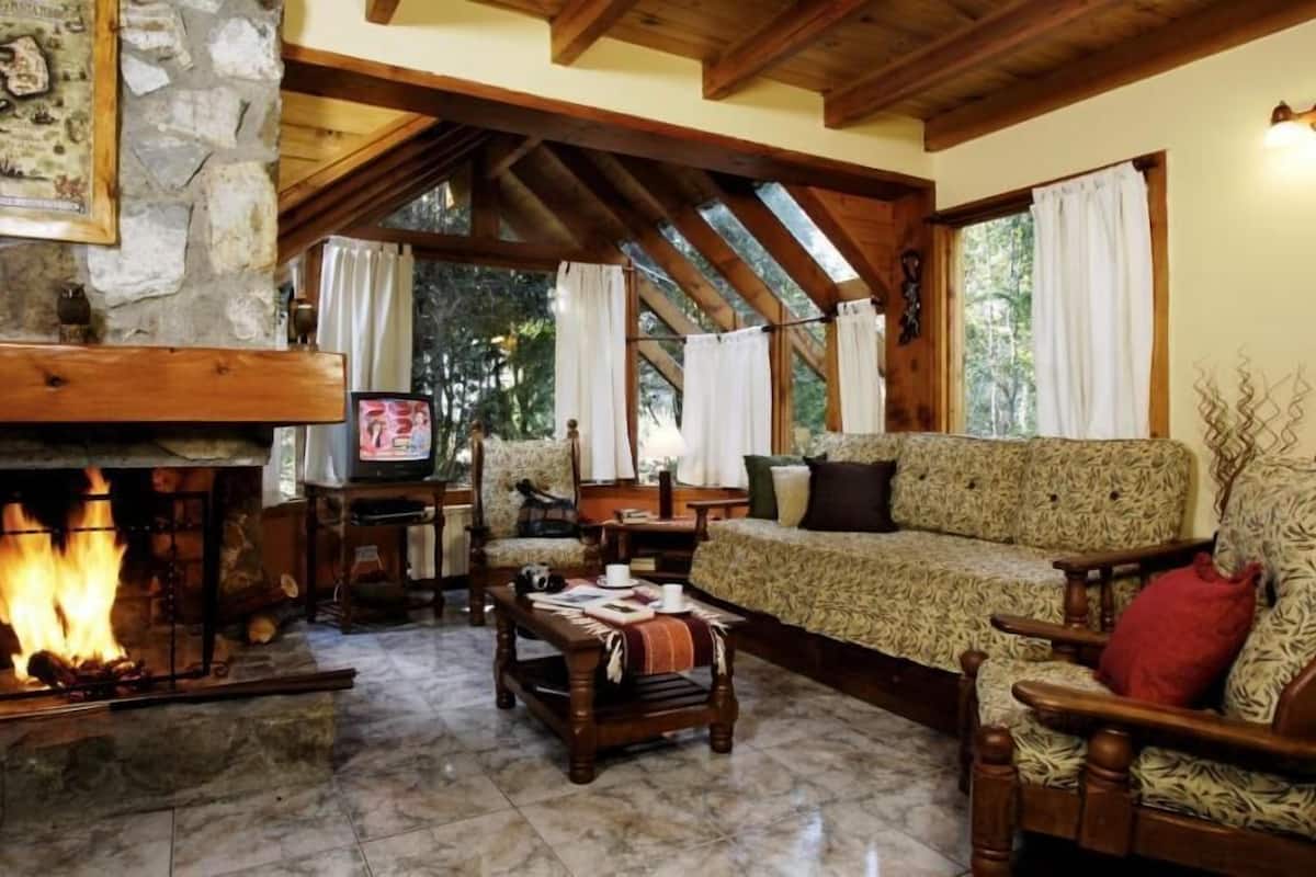 A cozy living room with a stone fireplace, wooden beams, a sofa, and a television.