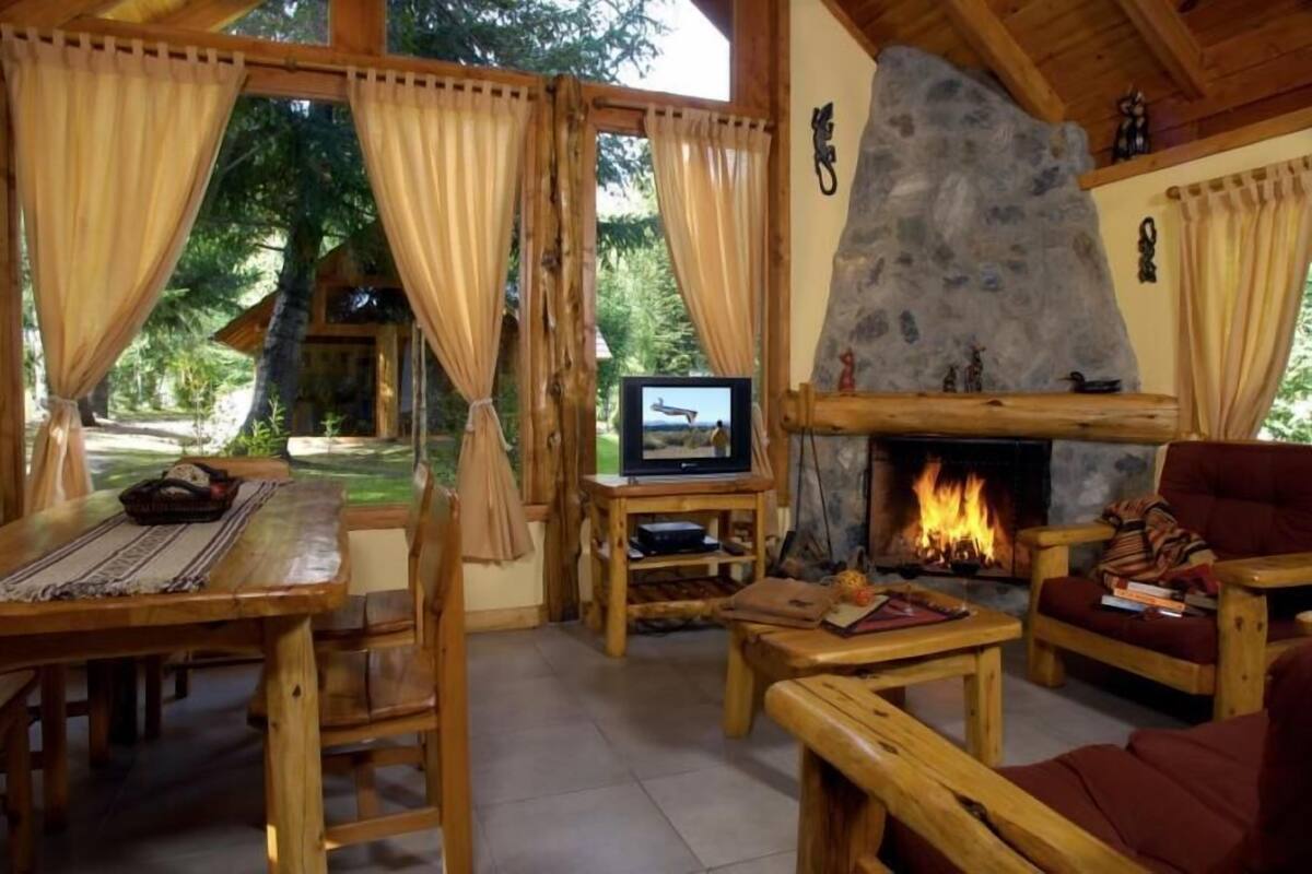A cozy lodge interior with a stone fireplace, wooden furniture, and a television on a wooden stand.