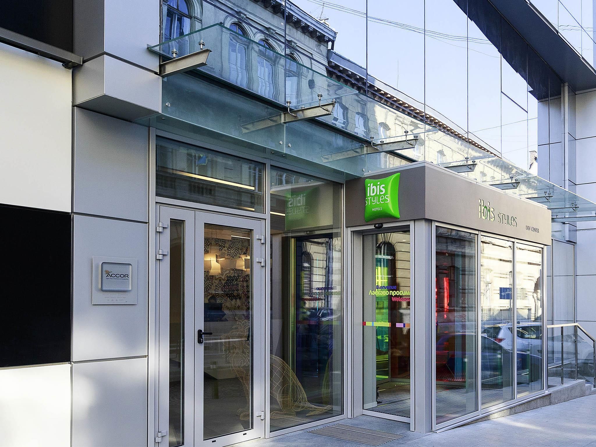 Entrada de hotel com fachada de vidro, uma placa verde indicando 'ibis Styles Hotels' e o logotipo da ACCOR visível.