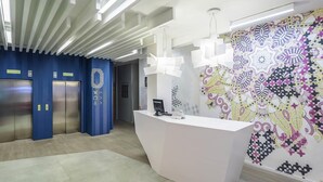 A modern reception area with a white reception desk, two elevators, and a patterned wall. - Ibis Styles Lviv Center (Lviv)