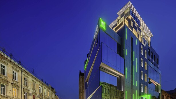 A modern hotel with a glass facade, a prominent green sign, and a street view with parked cars and pedestrians. - Ibis Styles Lviv Center (Lviv)
