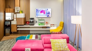 A modern hotel room with a flat-screen TV displaying a weather forecast, a desk with a coffee machine, a bright yellow armchair, and a pink sofa with a patterned pillow. - Ibis Styles Lviv Center (Lviv)