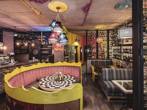 A bar area with a checkered table, seating with striped cushions, and shelves with bottles. - Ibis Styles Lviv Center (Lviv)