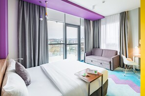 A modern hotel room with a large bed, a sofa, a desk, and a view of the city through large windows. - Ibis Styles Lviv Center (Lviv)