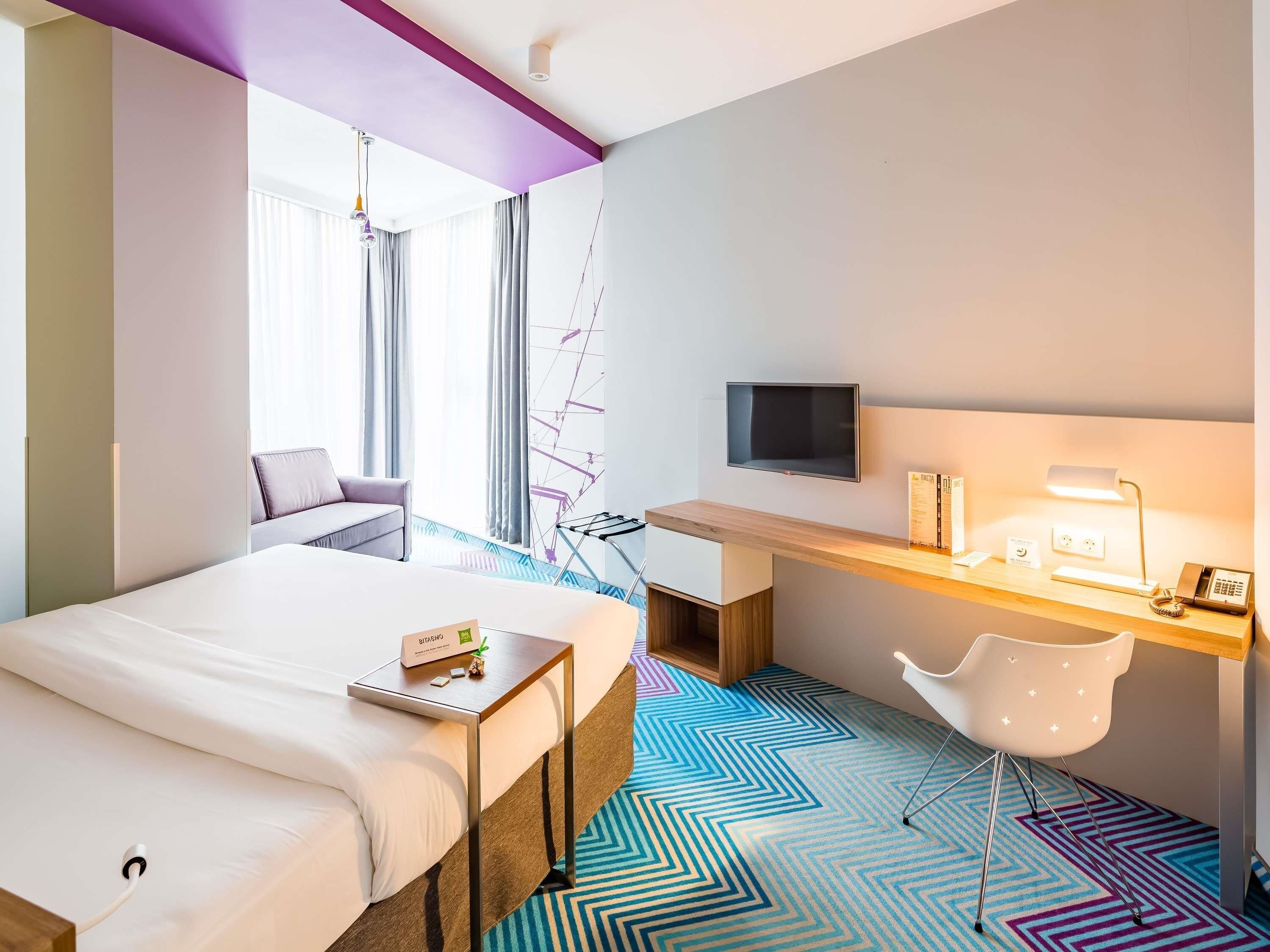 A hotel room with a bed, a desk with a computer, a TV, and a chair.