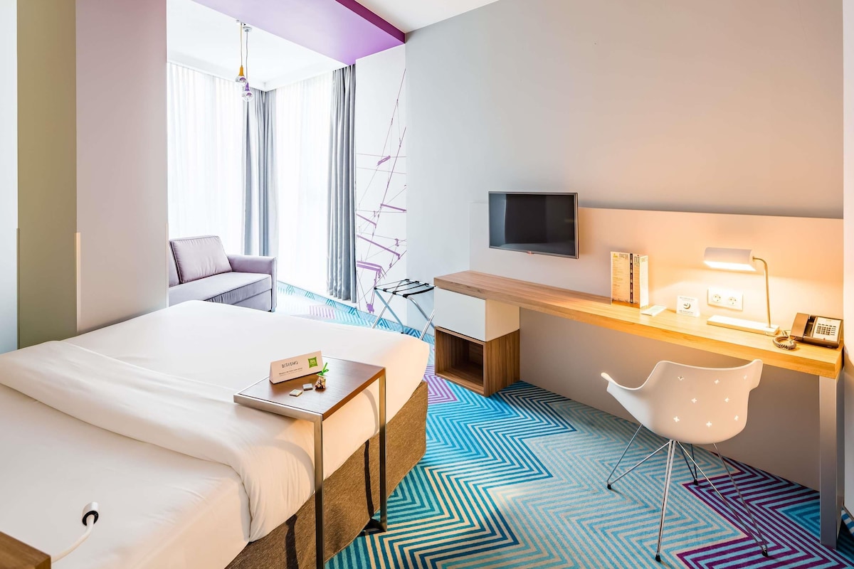 Una habitación de hotel con una cama, un escritorio con ordenador, un televisor y una silla.
